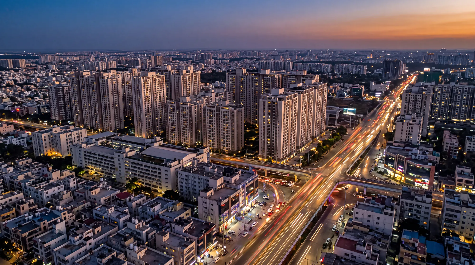 Aerial view of Bengaluru at blue hour with high-rise residential towers and light trails on a wide road