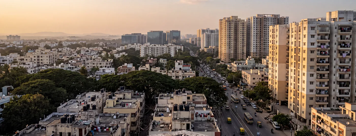 Bengaluru at golden hour: new apartment towers, a busy road and rain trees